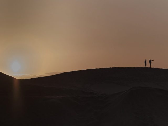 Silhouette de deux personnes explorant la crête d'une dune de sable lors d'un coucher de soleil brumeux