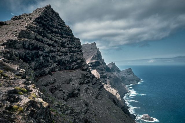 Falaises rocheuses escarpées et spectaculaires plongeant dans l'océan bleu sous un ciel nuageux