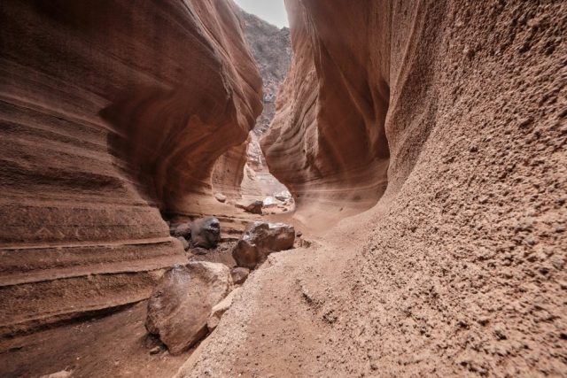 Formation géologique d'un canyon étroit aux parois de roches rouges striées et lisses avec un sol rocheux