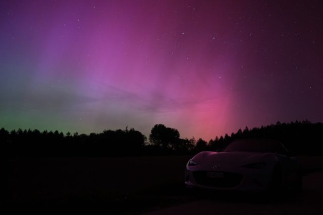 Voiture de sport blanche en silhouette garée de nuit sous un ciel étoilé et des aurores boréales roses