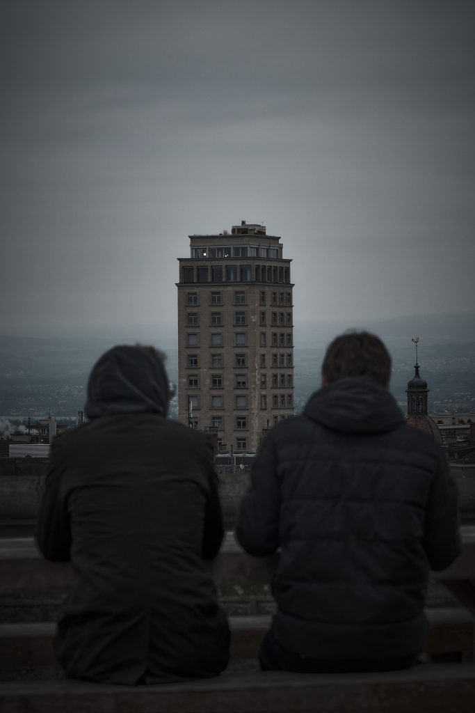 Deux personnes vues de dos observant au loin la Tour Bel-Air à Lausanne sous un ciel gris, photographie urbaine à l'ambiance sombre.
