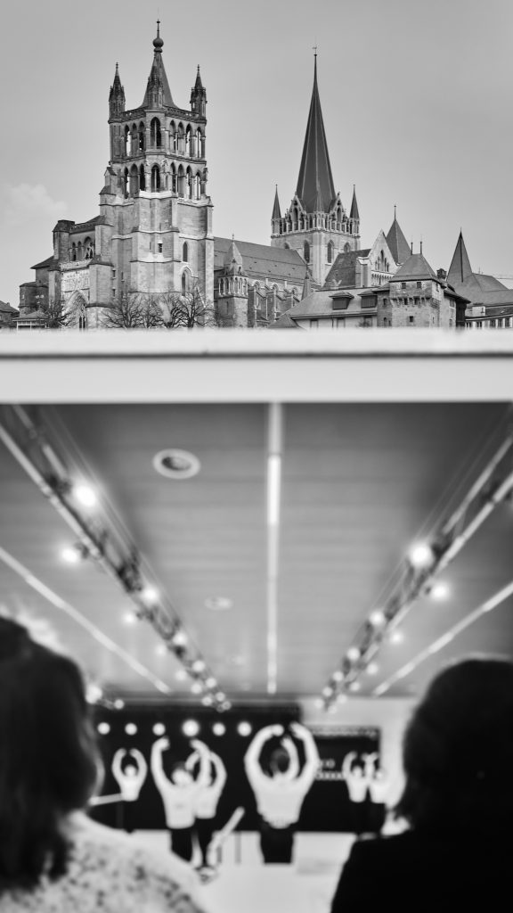 Composition photographique avec la Cathédrale de Lausanne en noir et blanc dans la partie supérieure, et le reflet de personnes dansant en intérieur dans la partie inférieure.