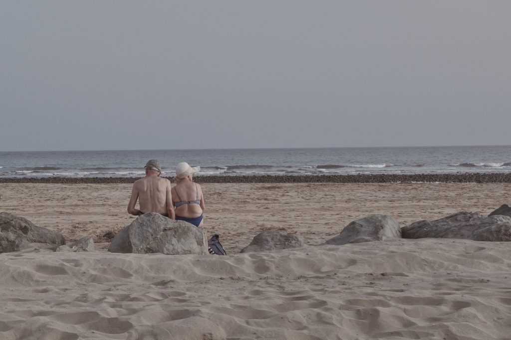Couple en maillot de bain assis de dos sur des rochers sur une plage de sable, regardant les vagues de l'océan.