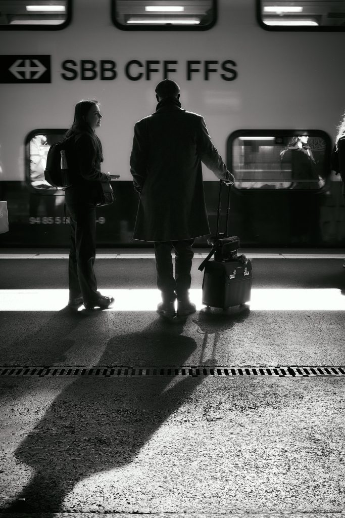 Passagers avec valises attendant sur le quai devant un train SBB CFF FFS en noir et blanc.
