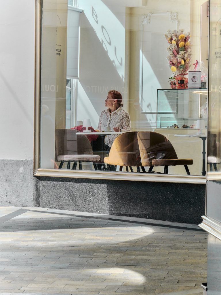 Femme attablée prenant un café, vue à travers la vitrine lumineuse d'une boulangerie-pâtisserie.