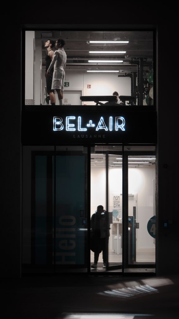 Façade nocturne illuminée de la salle de sport fitness Bel-Air à Lausanne avec des membres s'entraînant à l'étage.
