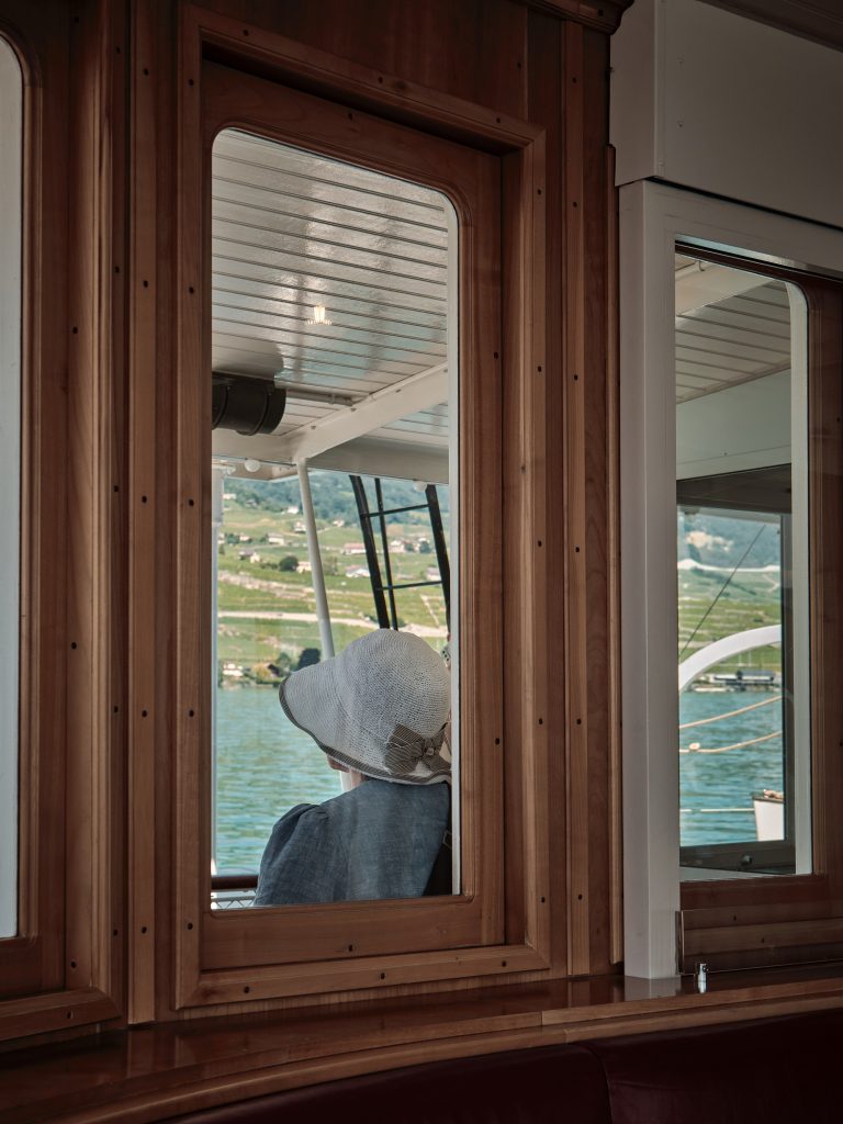 Passager portant un chapeau de paille admirant les vignobles en terrasses depuis la fenêtre d'un bateau en bois sur le lac.