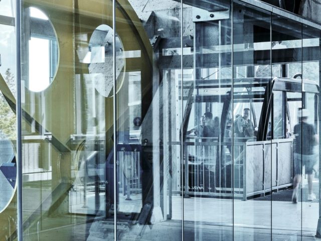 Reflets sur la verrière d'une station de téléphérique moderne avec passagers et machinerie.
