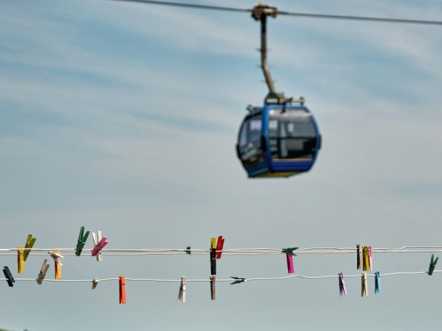 Pinces à linge colorées sur un fil au premier plan et cabine de téléphérique floue en arrière-plan.