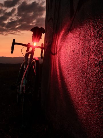 Silhouette de vélo de course et halo lumineux rouge sur un mur lors d'un crépuscule en nature.