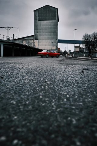 Perspective au sol sur un véhicule rétro rouge au pied d'un bâtiment d'usine désaffectée.