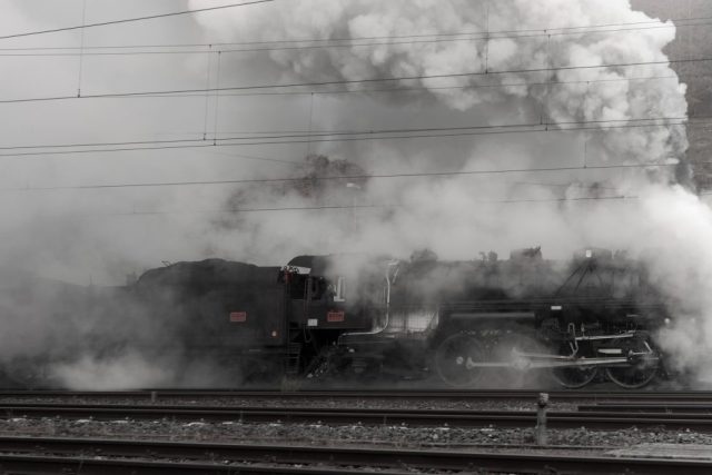 Gros plan latéral d'une locomotive à vapeur historique enveloppée dans un nuage de fumée grise.