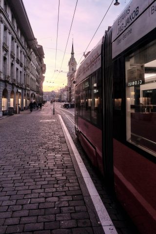 Tramway rouge circulant sur des pavés dans une rue historique de Berne au coucher du soleil.