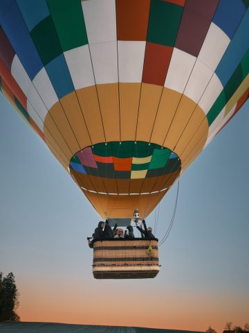 Montgolfière multicolore transportant des passagers dans sa nacelle au décollage lors d'un lever de soleil.
