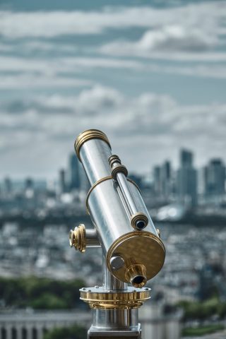 Télescope d'observation public en laiton et argent avec vue floutée sur la ville de Paris en arrière-plan.