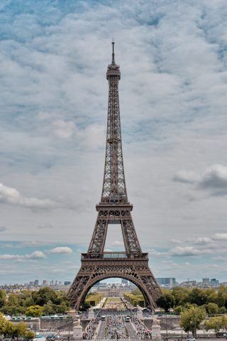 Vue symétrique de la Tour Eiffel à Paris depuis le Trocadéro sous un ciel nuageux, dominant le Champ de Mars.