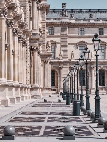 Alignement en perspective de réverbères noirs traditionnels le long de la façade sculptée du Musée du Louvre à Paris.