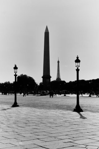 Photo en noir et blanc de l'Obélisque de Louxor et de la Tour Eiffel au loin, encadrés par deux réverbères sur la place de la Concorde à Paris.