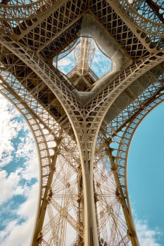 Vue géométrique de l'intérieur des piliers et des arches de la Tour Eiffel se détachant sur un ciel bleu.