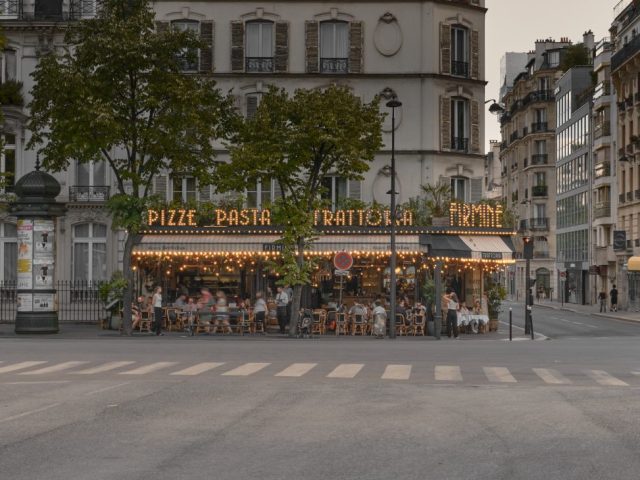 Façade illuminée de la trattoria italienne Firmin à Paris à la nuit tombante, avec des clients installés en terrasse.
