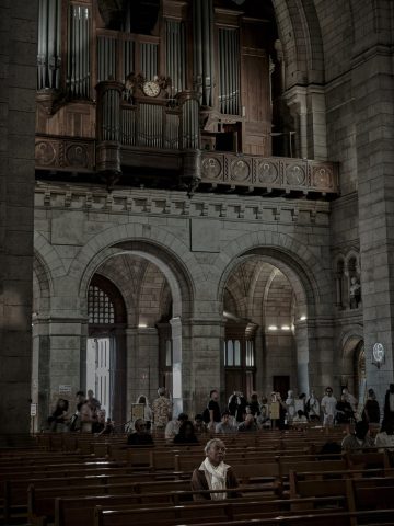 Intérieur d'une église en pierre à Paris montrant la tribune des grandes orgues en bois et des visiteurs assis sur les bancs.