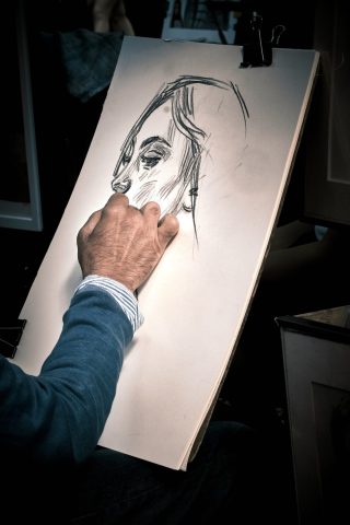 Gros plan sur la main d'un dessinateur réalisant un portrait de femme au fusain sur un chevalet à Montmartre.