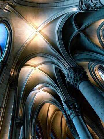 Architecture gothique montrant les voûtes d'ogives et les colonnes sculptées d'une cathédrale parisienne éclairée de bleu.