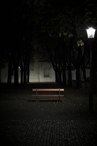 Photographie nocturne d'un banc en bois isolé et éclairé par un lampadaire classique dans un parc sombre