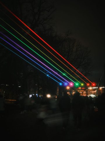 Foule observant un spectacle nocturne avec de puissants faisceaux laser aux couleurs de l'arc-en-ciel projetés dans le ciel