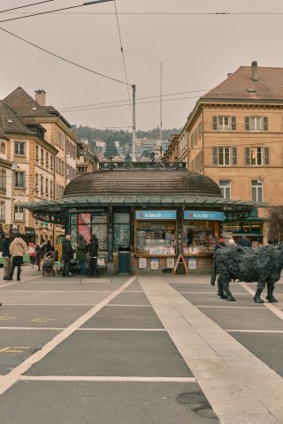 Place urbaine animée avec un pavillon k kiosk traditionnel et une sculpture de vache noire, architecture typique en arrière-plan