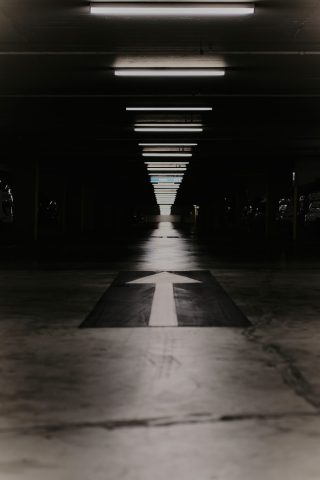 Flèche directionnelle blanche peinte au sol dans un parking souterrain sombre, avec des néons au plafond créant un effet de perspective.