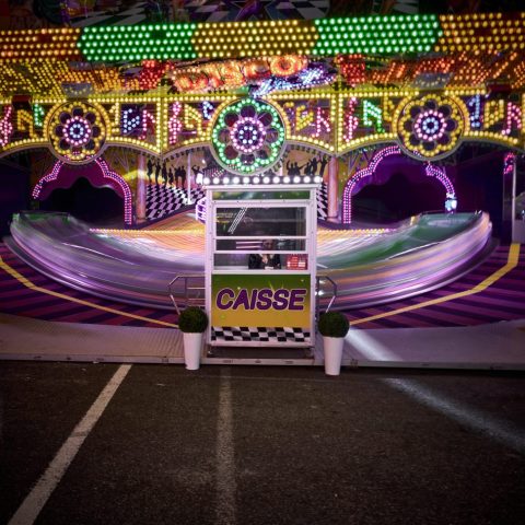 Caisse de manège coloré dans une fête foraine nocturne avec éclairages néon vifs et flou de mouvement illustrant la vitesse des nacelles.