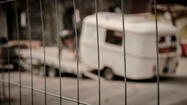 Vue à travers un grillage métallique net d'une caravane blanche vintage floue en train d'être chargée sur une remorque.