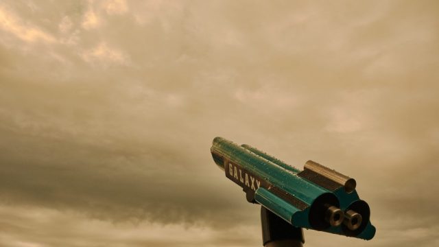 Télescope touristique bleu avec l'inscription Galaxy, couvert de gouttes de pluie et pointé vers un ciel nuageux et sombre.