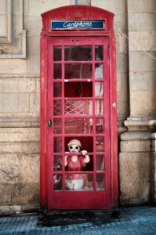 Enfant avec des lunettes de soleil rigolotes regardant à travers la vitre d'une authentique cabine téléphonique rouge Cardphone à Malte.